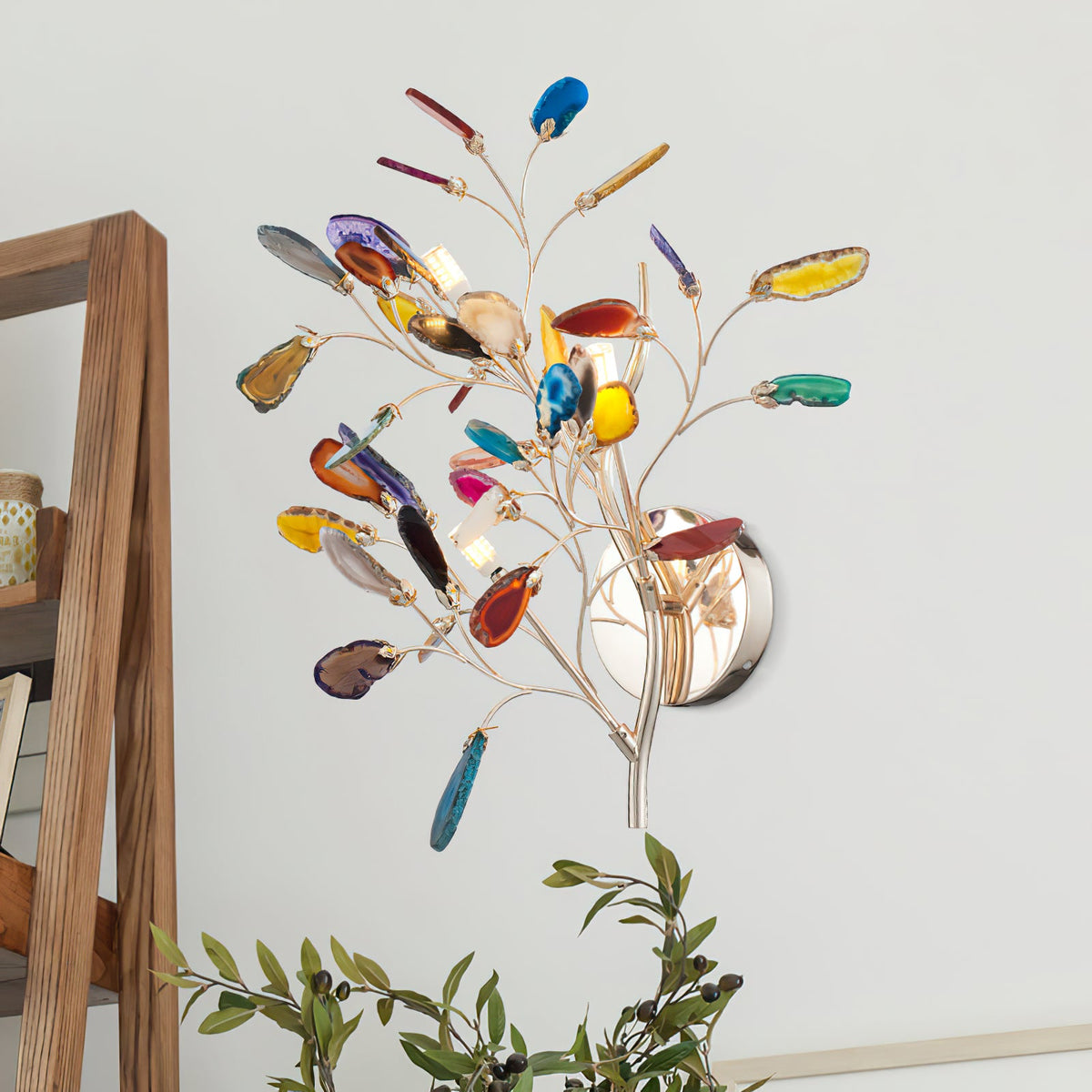 This Clérachic agate wall light on a white wall beside a wooden frame, its stone slices in orange, blue and green.