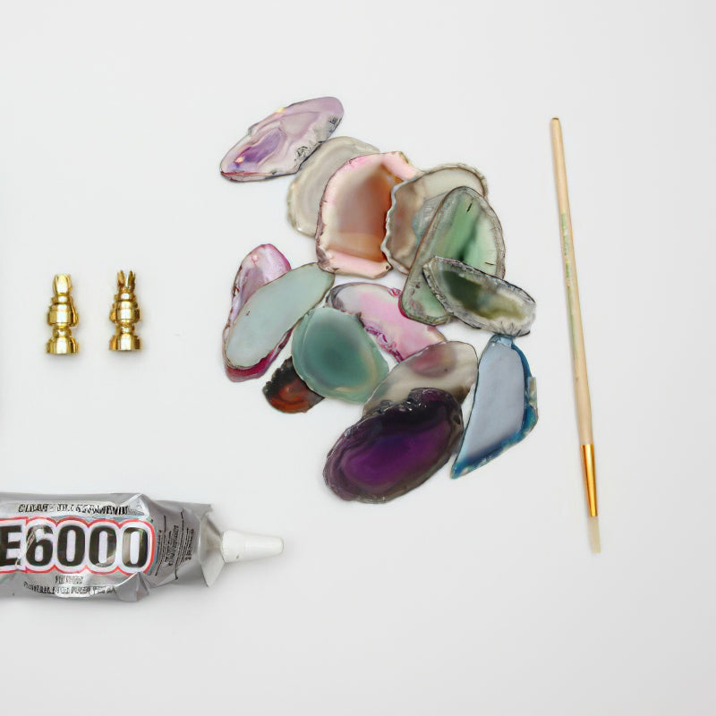 Loose agate slices in green, purple and pink laid out with two brass fittings, a thin brush and a tube of clear glue for this Clérachic wall light.
