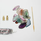 Loose agate slices in green, purple and pink laid out with two brass fittings, a thin brush and a tube of clear glue for this Clérachic wall light.