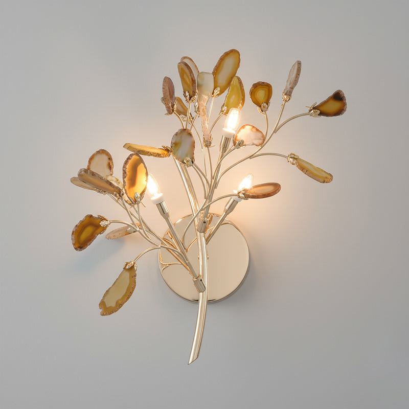 Yellow Clérachic agate wall light lit on a grey wall, its honey-coloured slices glowing around three candle-style bulbs.