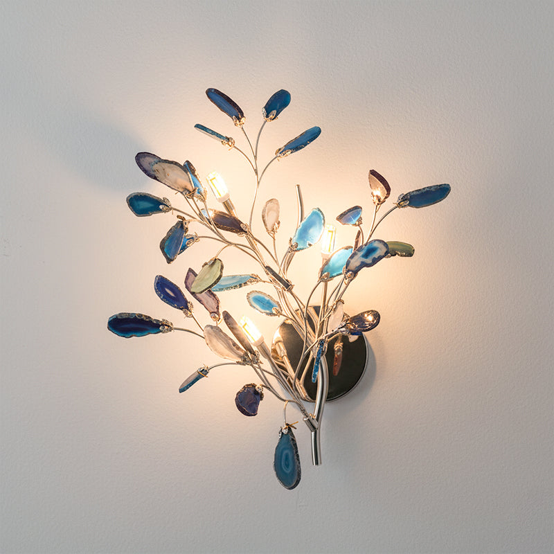 A larger blue Clérachic agate wall light lit on a pale wall, with teal and navy slices around four candle-style bulbs.