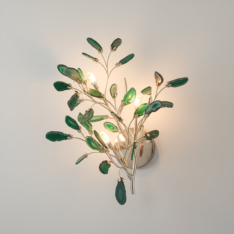 Larger green Clérachic agate wall light lit on a pale wall, with dark green slices around four candle-style bulbs.