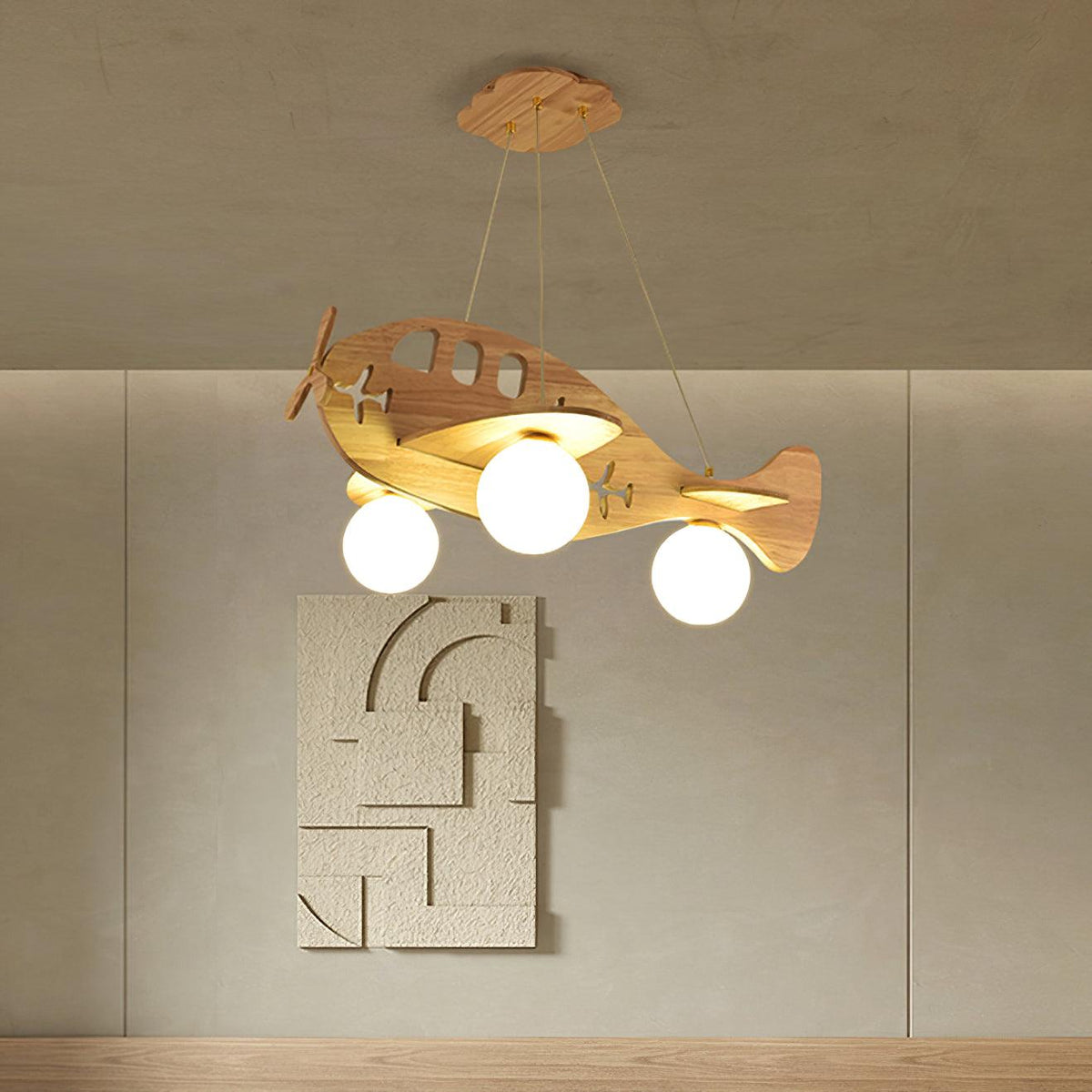 Close view of the Clérachic wooden airplane light, its three globes glowing, against a taupe wall with a textured relief panel.