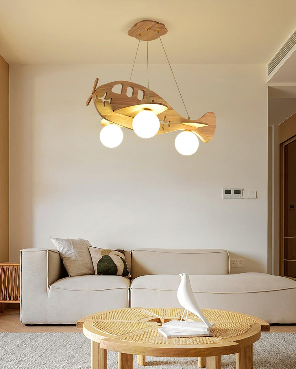 Clérachic wooden airplane light switched on in a living room, above a cream sofa and a round rattan coffee table.