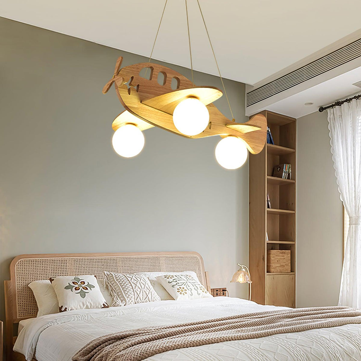 Clérachic airplane pendant above a bed with a rattan headboard and a beige throw, in a room with a sage green wall.