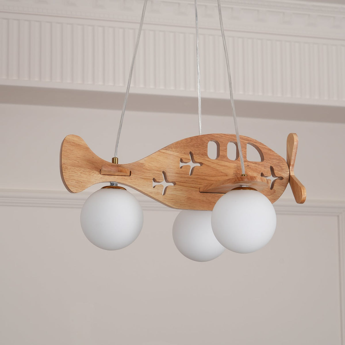 Close view of the Clérachic airplane light from below, with three unlit white globes and the cut-out windows on its wooden body.