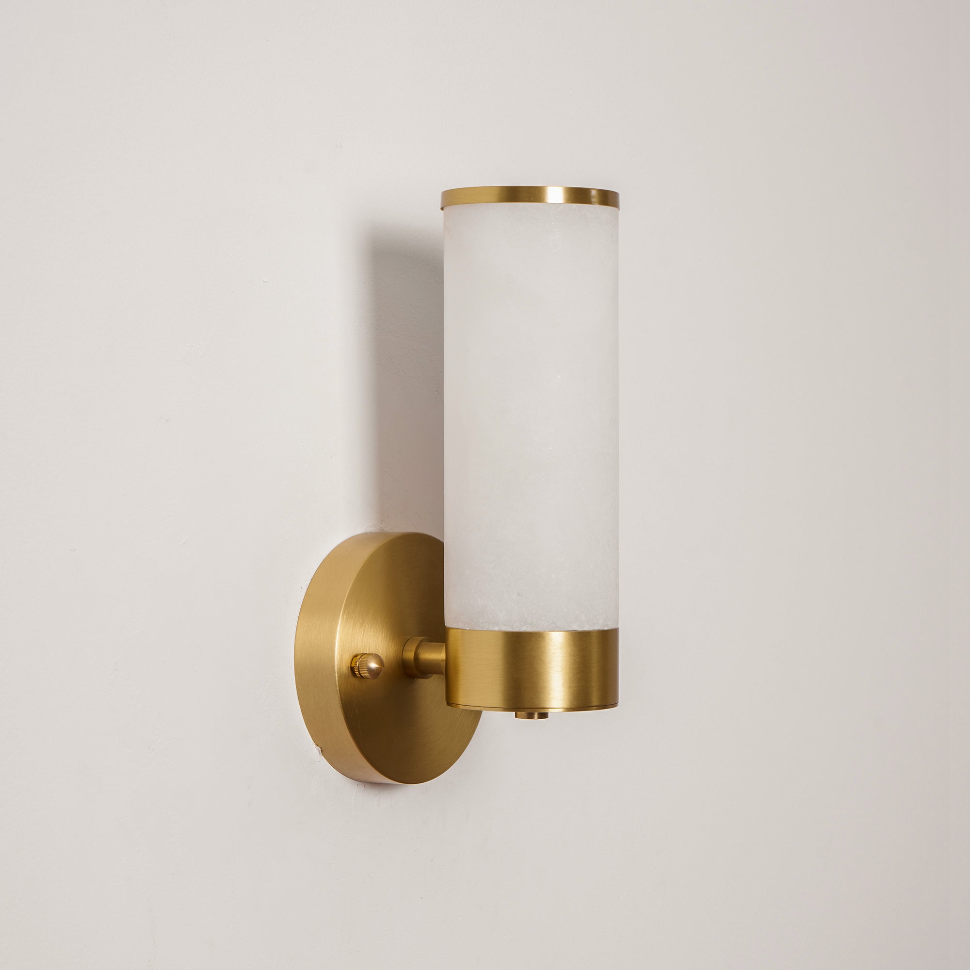 Angled view of the Clérachic Alabaster and Brass Wall Sconce, short arm and knurled thumbscrew clear against a pale wall.