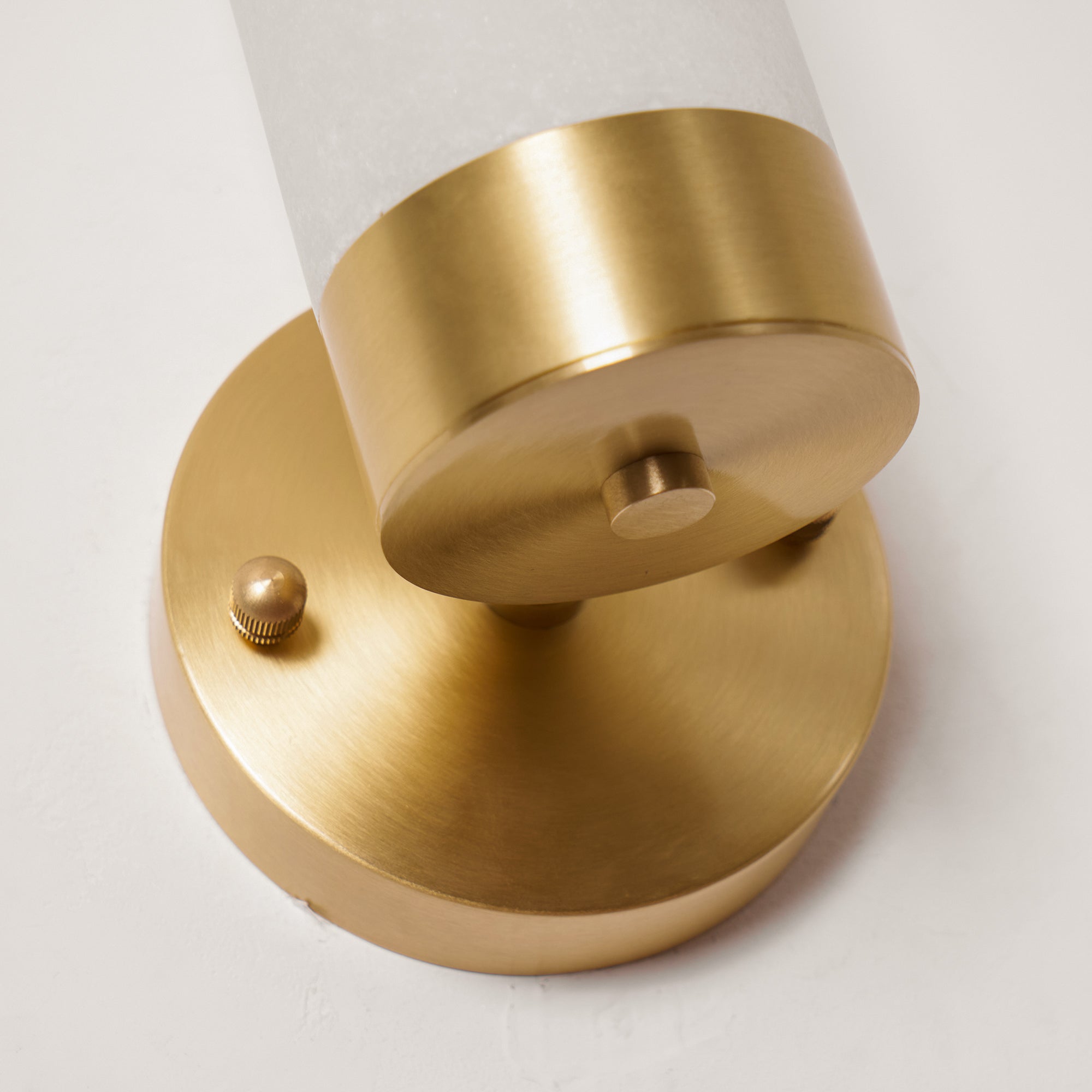 Close-up of the Clérachic Alabaster and Brass Wall Sconce hardware: brushed backplate, stub arm and knurled thumbscrew.