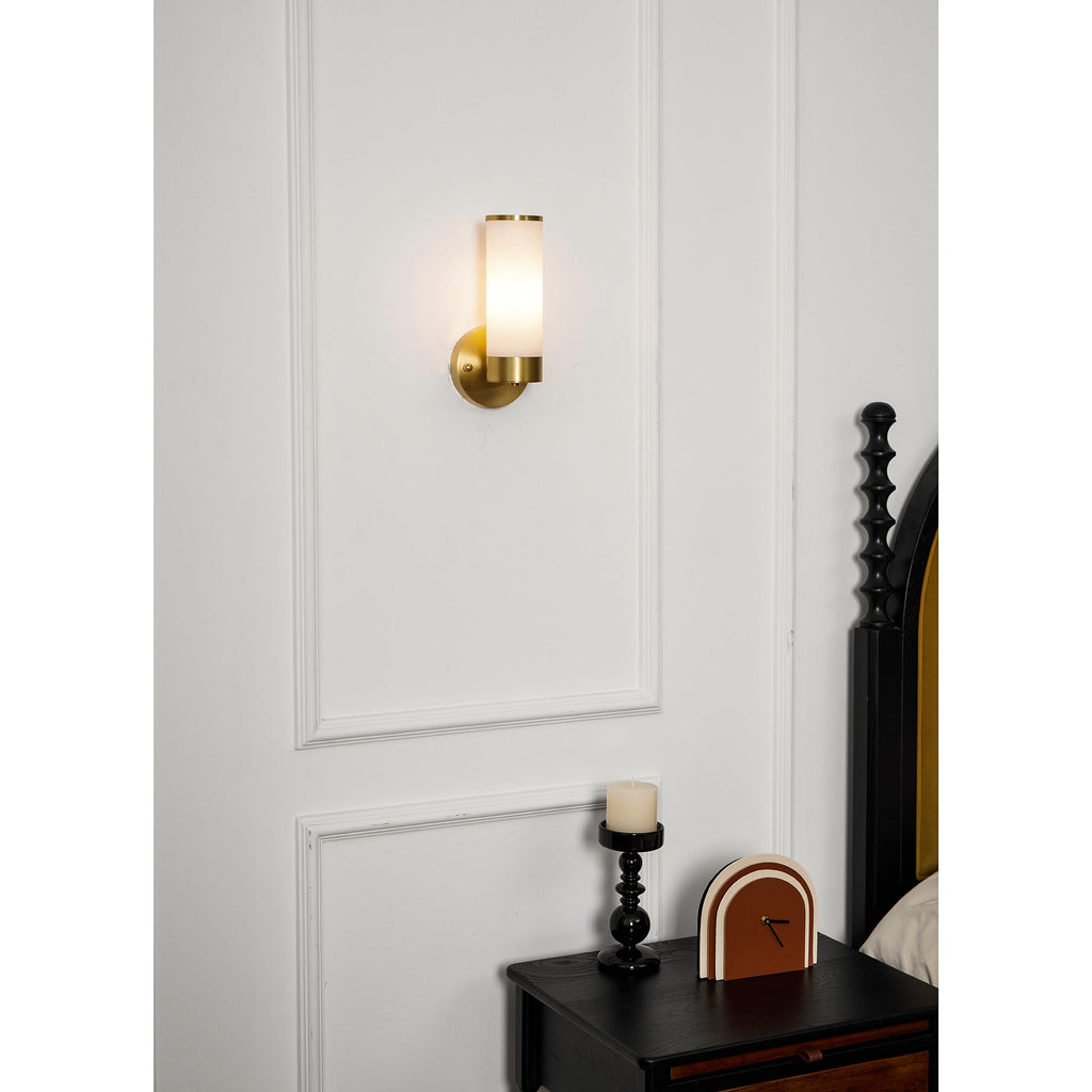 Clérachic Alabaster and Brass Wall Sconce glowing on a panelled bedroom wall, its light pooling across the moulding.