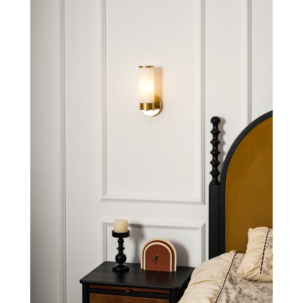 Clérachic Alabaster and Brass Wall Sconce at bedside height, warm light on the wall above a candle and a small clock.