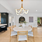 Clérachic Alabaster Bead Chandelier in brass above a round white dining table, lighting an open kitchen with dark cabinetry.