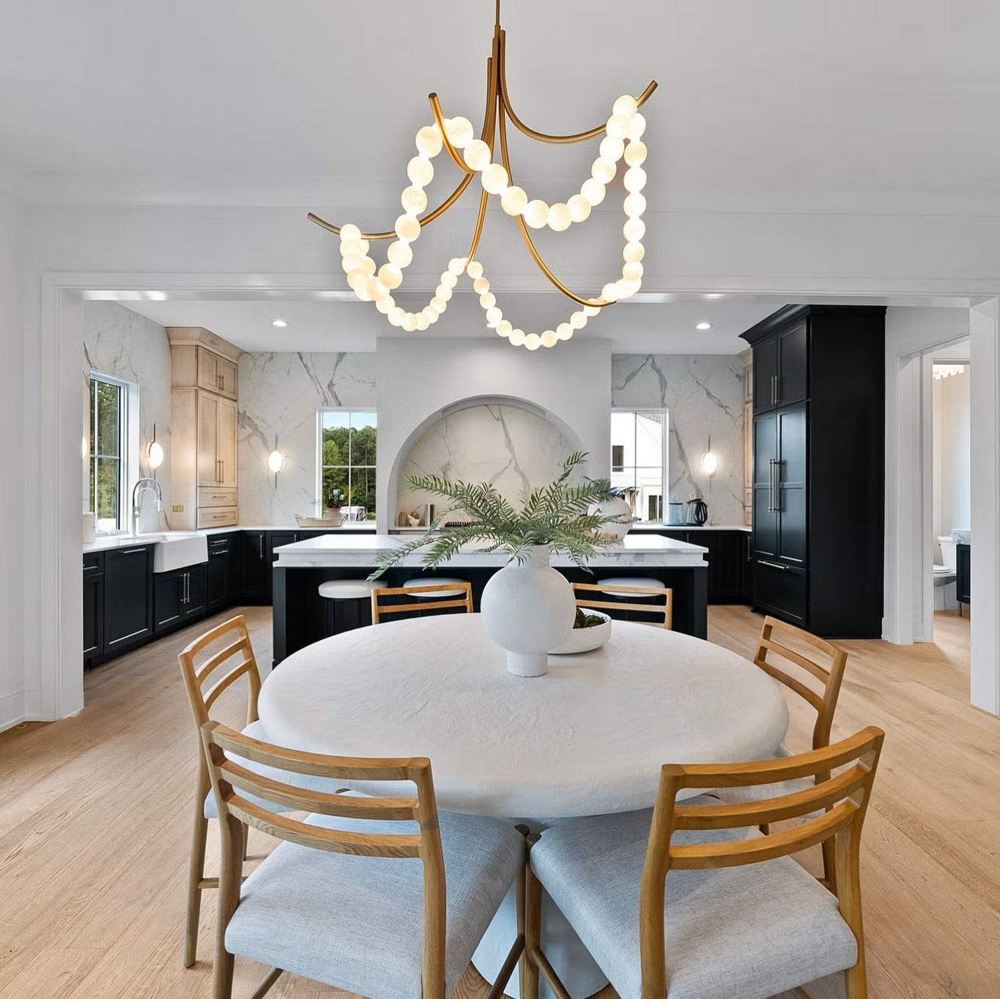 Wide view of the Clérachic Alabaster Bead Chandelier lighting a round dining table set against a marble kitchen beyond.