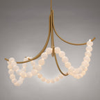 Clérachic Alabaster Bead Chandelier in brass on a grey studio backdrop, arms sweeping out under looping alabaster swags.