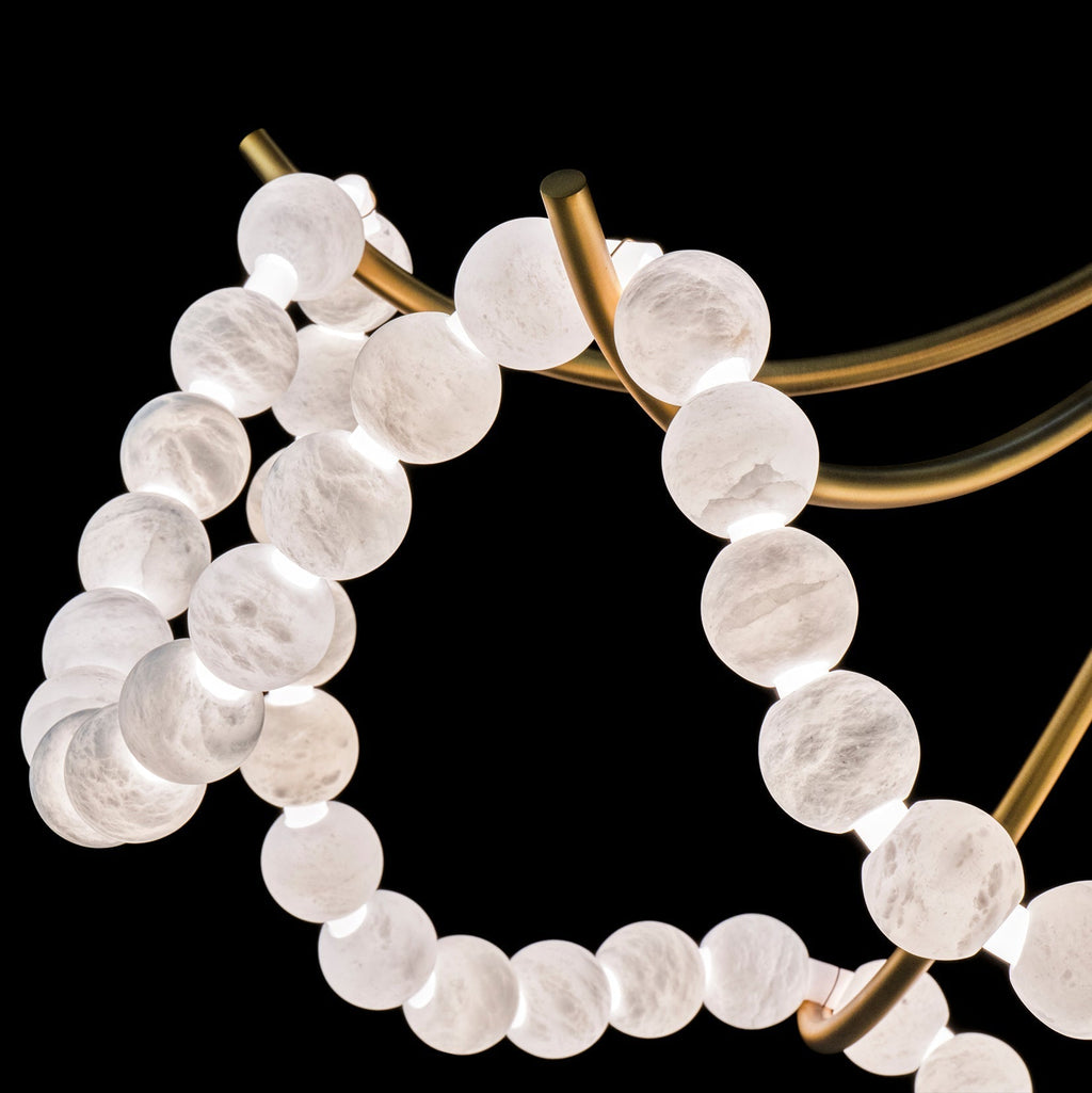 Detail of a brass arm and bead strands on the Clérachic Alabaster Bead Chandelier, the cut stone veined and softly lit.