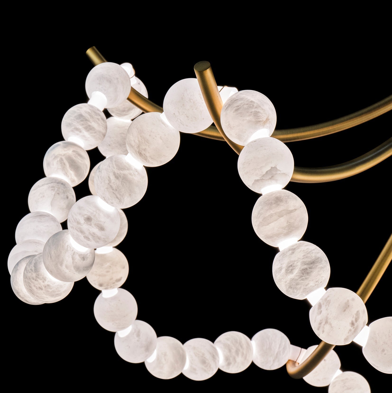 Detail of a brass arm and bead strands on the Clérachic Alabaster Bead Chandelier, the cut stone veined and softly lit.