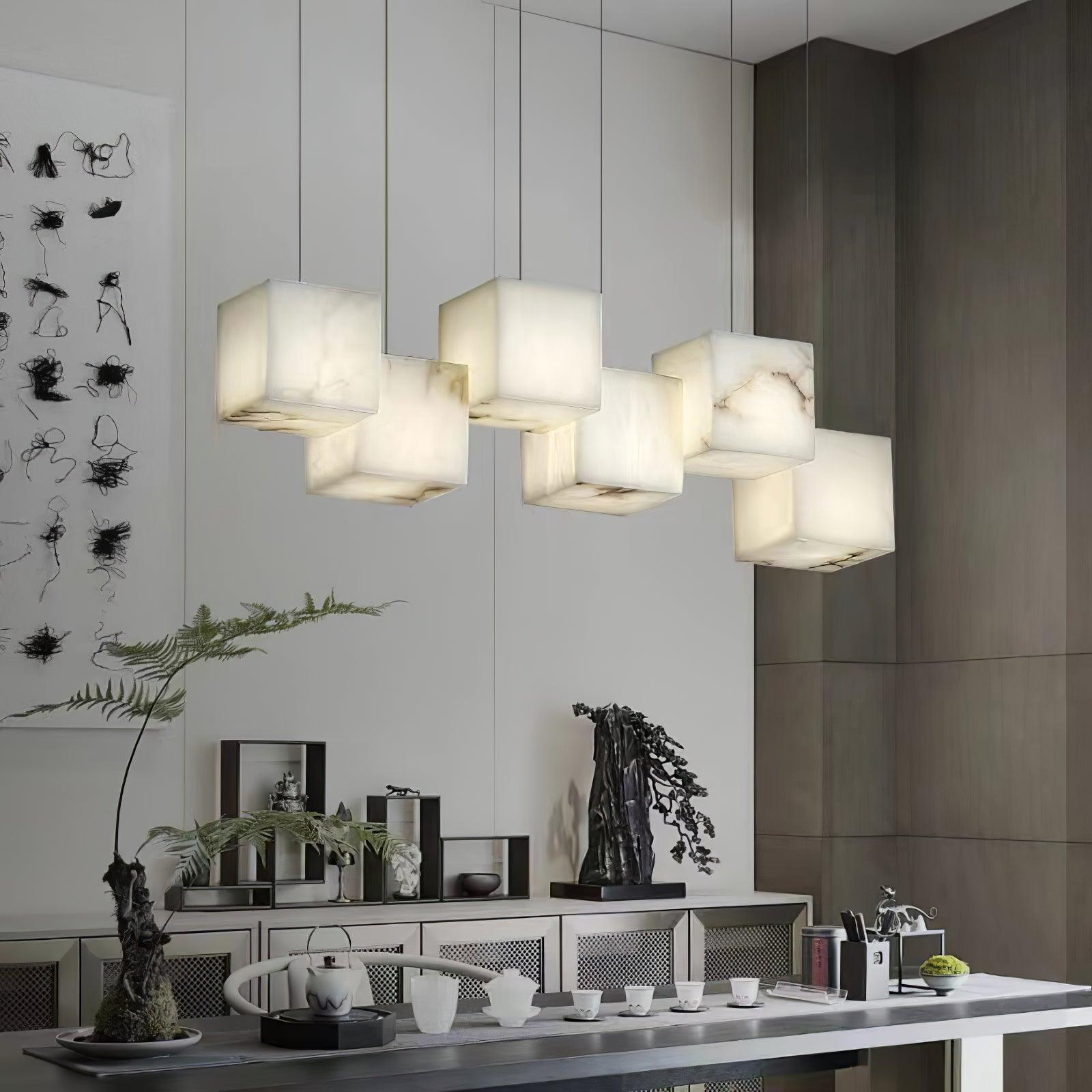 Clérachic box chandelier lit above a sideboard with ferns and a tea set below.