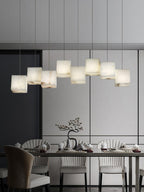 Clérachic box pendant lit over a long dining table in a pale grey panelled room.