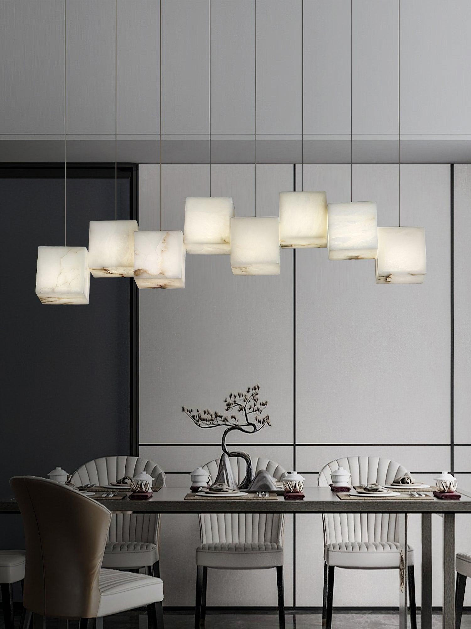 Clérachic box pendant lit over a long dining table in a pale grey panelled room.