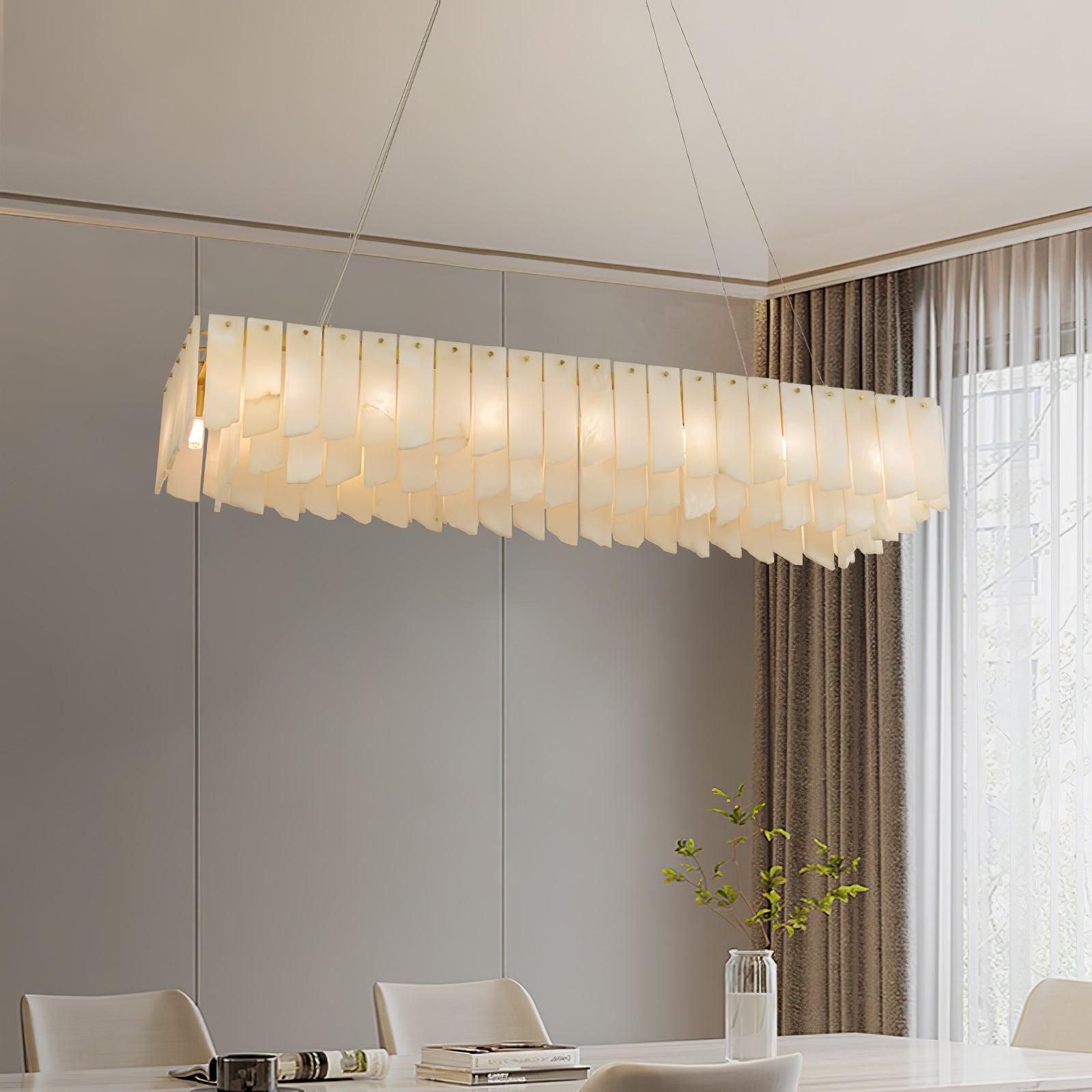 Clérachic cascade chandelier lit above a pale dining table beside floor-length curtains.