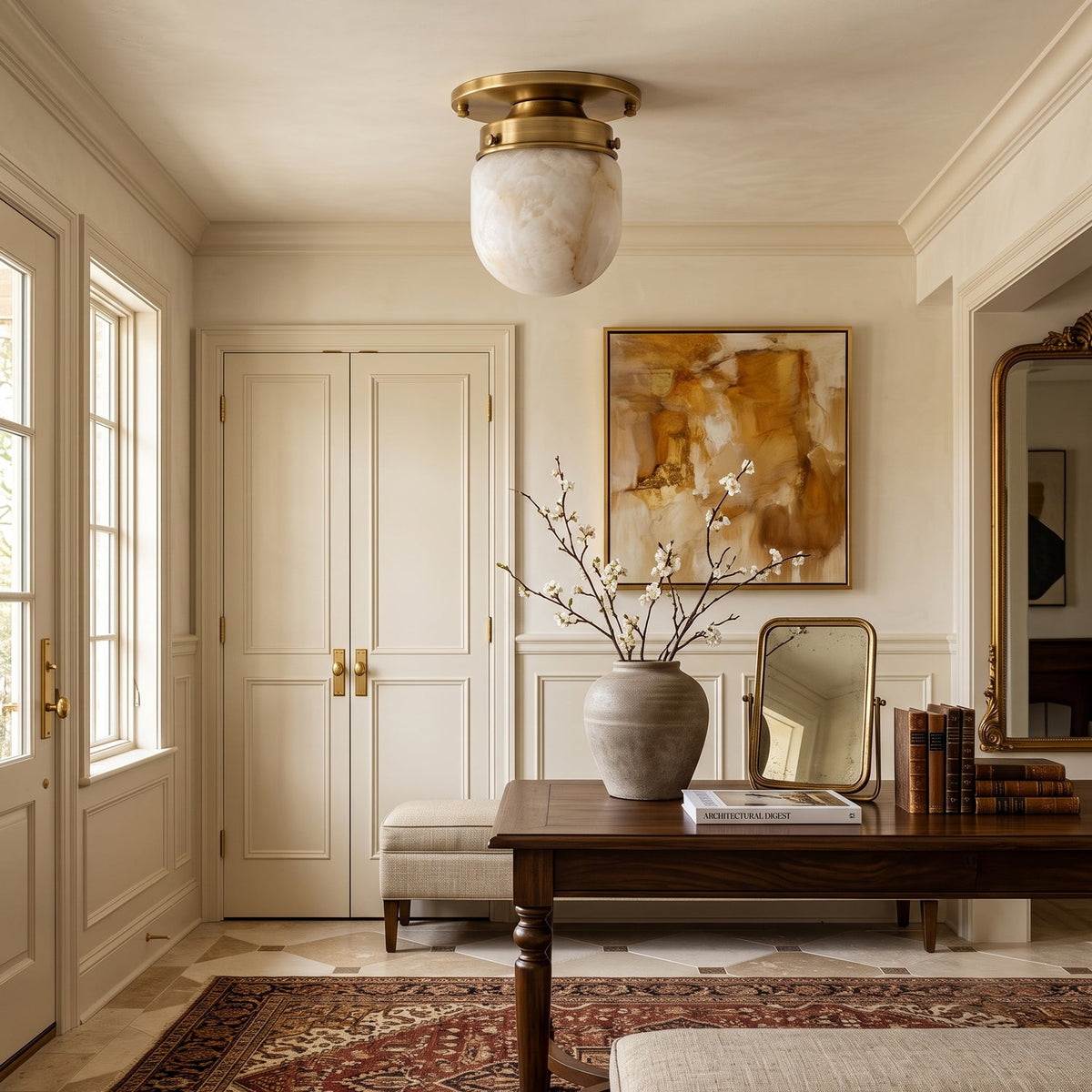 In a cream-panelled entry, this Clérachic flush mount sits above a dark wood table with a stone vase and a gilt mirror.