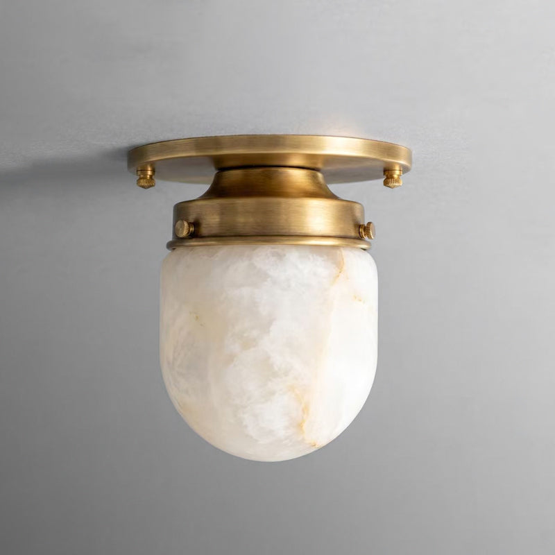 Close view of the white alabaster shade and brushed brass canopy on this Clérachic ceiling light, against a grey wall.