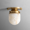 Close view of the white alabaster shade and brushed brass canopy on this Clérachic ceiling light, against a grey wall.