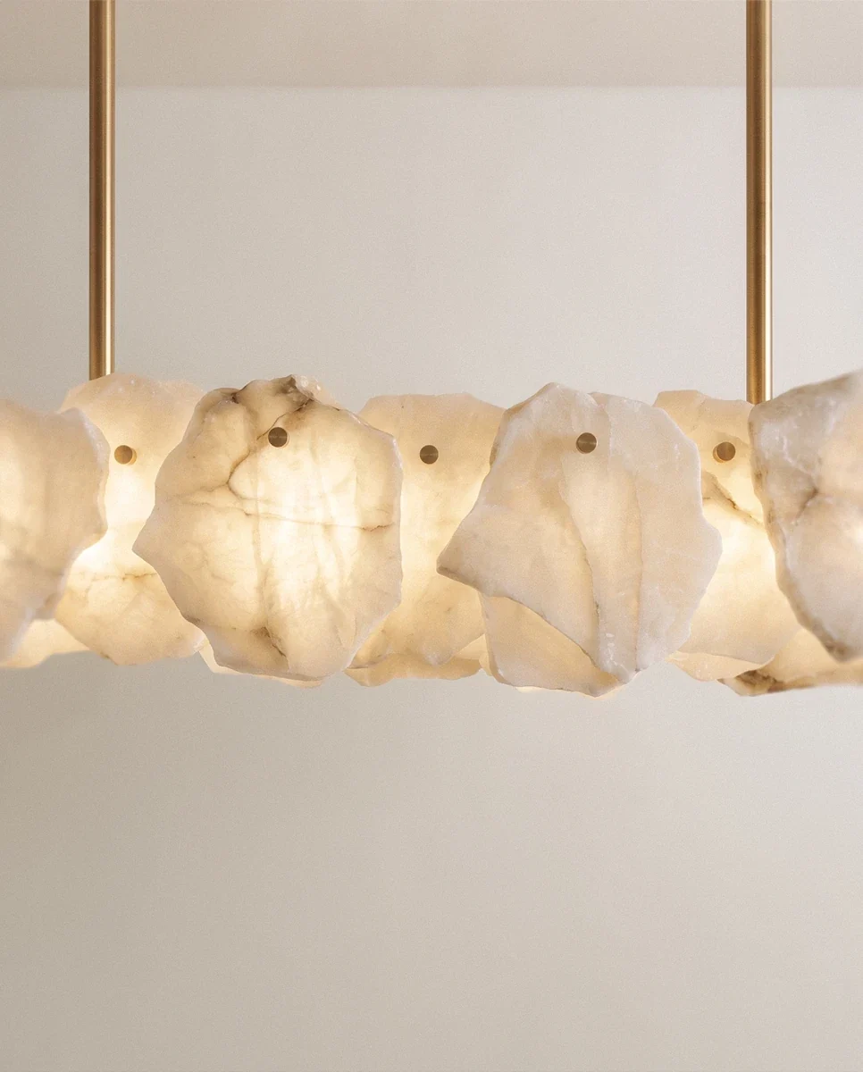 Clérachic linear chandelier close-up, glowing alabaster panels with brown veining, each held by a brass pin, two brass rods above.