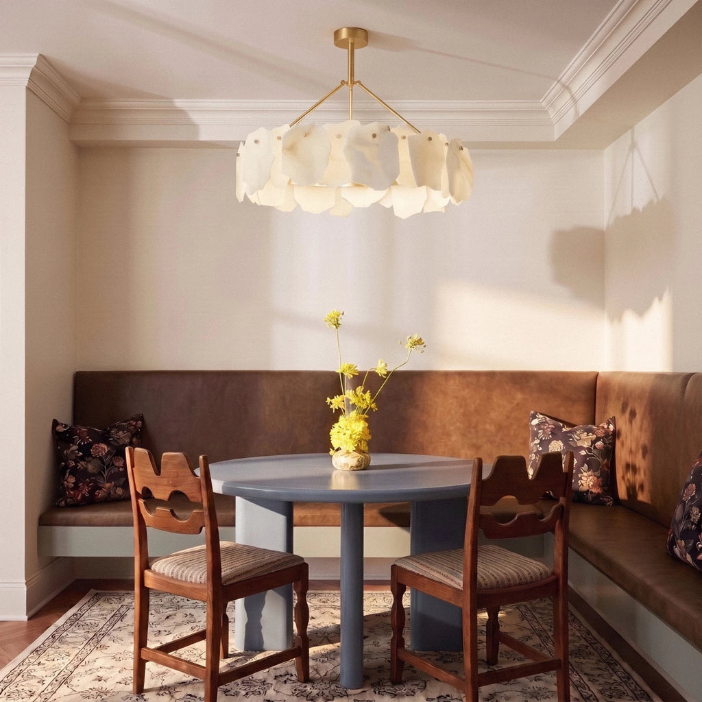 Clérachic round alabaster chandelier above a pale blue round table in a leather banquette dining nook with wooden chairs.