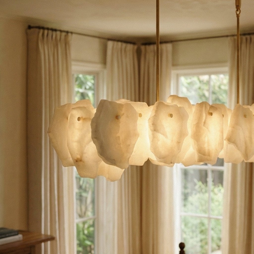 Clérachic linear chandelier close-up, warm-glowing alabaster panels and two brass rods in front of a window with soft curtains.