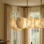 Clérachic linear chandelier close-up, warm-glowing alabaster panels and two brass rods in front of a window with soft curtains.
