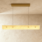 Clérachic rectangular alabaster pendant glowing warm gold on two thin cables from a brass ceiling plate, against a limewash wall.