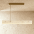 Clérachic long alabaster pendant lit softly, its pale veined stone face with four brass studs hanging from a brass ceiling bar.