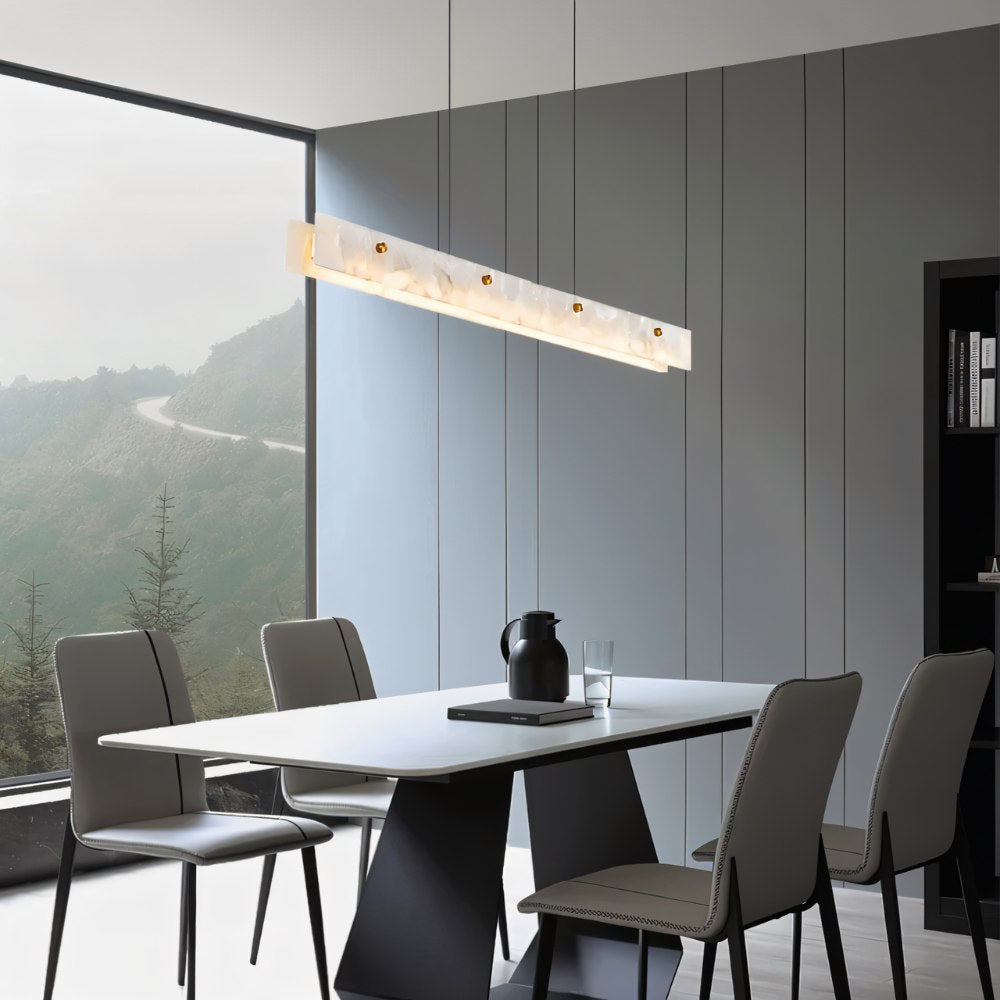 Clérachic linear alabaster pendant with brass studs hung above a white dining table, grey chairs and a misty hillside window.
