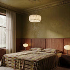 Clérachic alabaster ring chandelier in polished steel above a bed in a bedroom with olive plaster walls