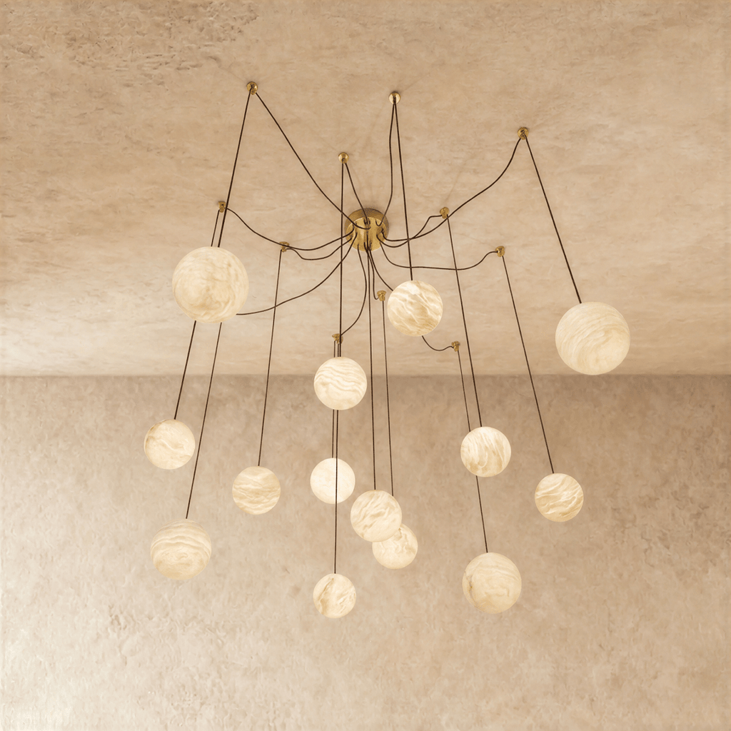 Clérachic spider-style chandelier of alabaster-look globes on long thin cords from a brass canopy, glowing against a limewash ceiling.