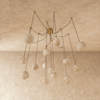 Clérachic spider-style chandelier of veined alabaster-look globes on long thin cords, shown unlit under a limewash ceiling.