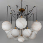 Clérachic chandelier of large veined alabaster-look globes on black cords from a brass canopy, shown unlit against a grey ceiling.