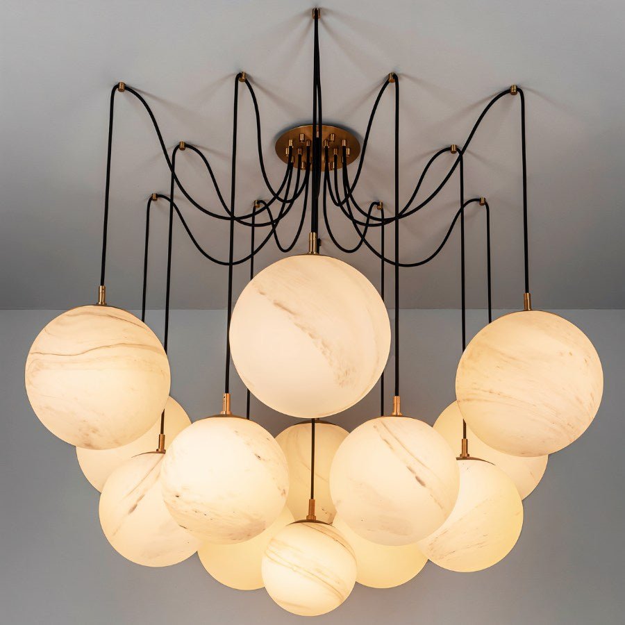 Clérachic chandelier of large veined alabaster-look globes on black cords from a brass canopy, glowing warm against a grey ceiling.