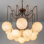 Clérachic chandelier of large veined alabaster-look globes on black cords from a brass canopy, glowing warm against a grey ceiling.
