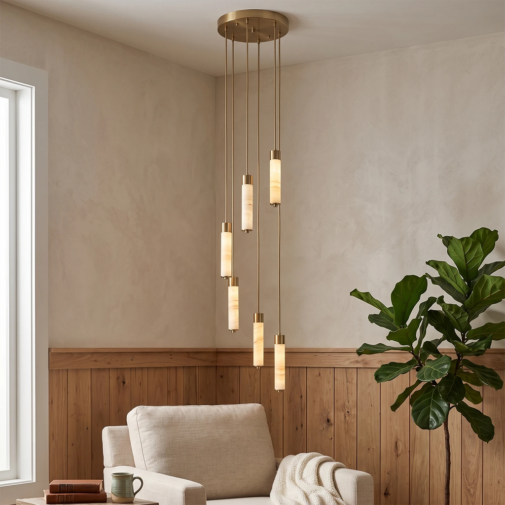 This Clérachic chandelier's brass-capped columns glow warm in a sitting-room corner beside an armchair and a fiddle-leaf fig.