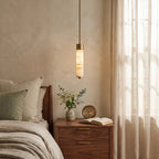 Close view of this Clérachic chandelier's fluted alabaster column glowing warm above a walnut bedroom nightstand.