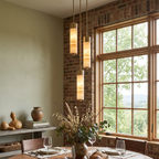 This Clérachic chandelier's brass-capped columns glow warm against an exposed brick wall beside a dining table set with gourds.