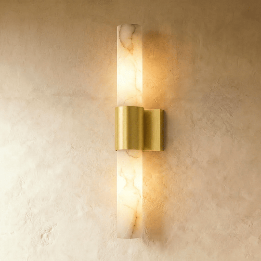 Clérachic 60 cm wall sconce with a veined alabaster column and brushed brass band, glowing warm on a limewash wall.