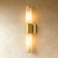 Clérachic 60 cm wall sconce with a veined alabaster column and brushed brass band, glowing warm on a limewash wall.