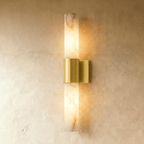 Clérachic 60 cm wall sconce with a veined alabaster column and brushed brass band, glowing warm on a limewash wall.