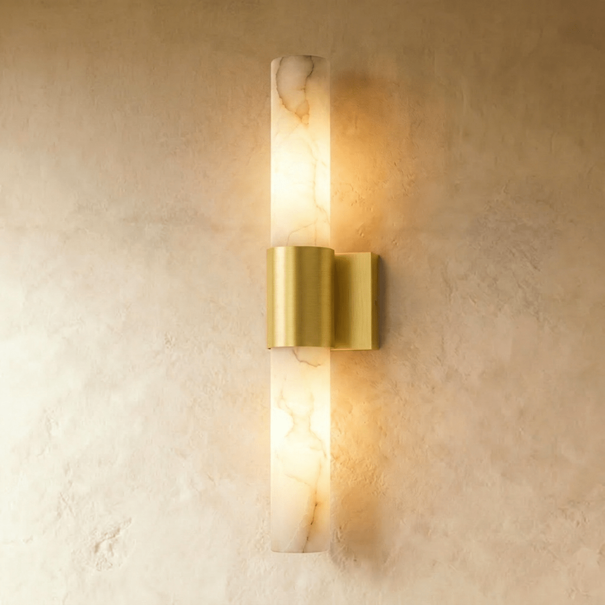 Clérachic 60 cm wall sconce with a veined alabaster column and brushed brass band, glowing warm on a limewash wall.