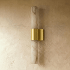 Clérachic wall sconce switched off, its pale veined alabaster column and brushed brass band on a limewash wall.