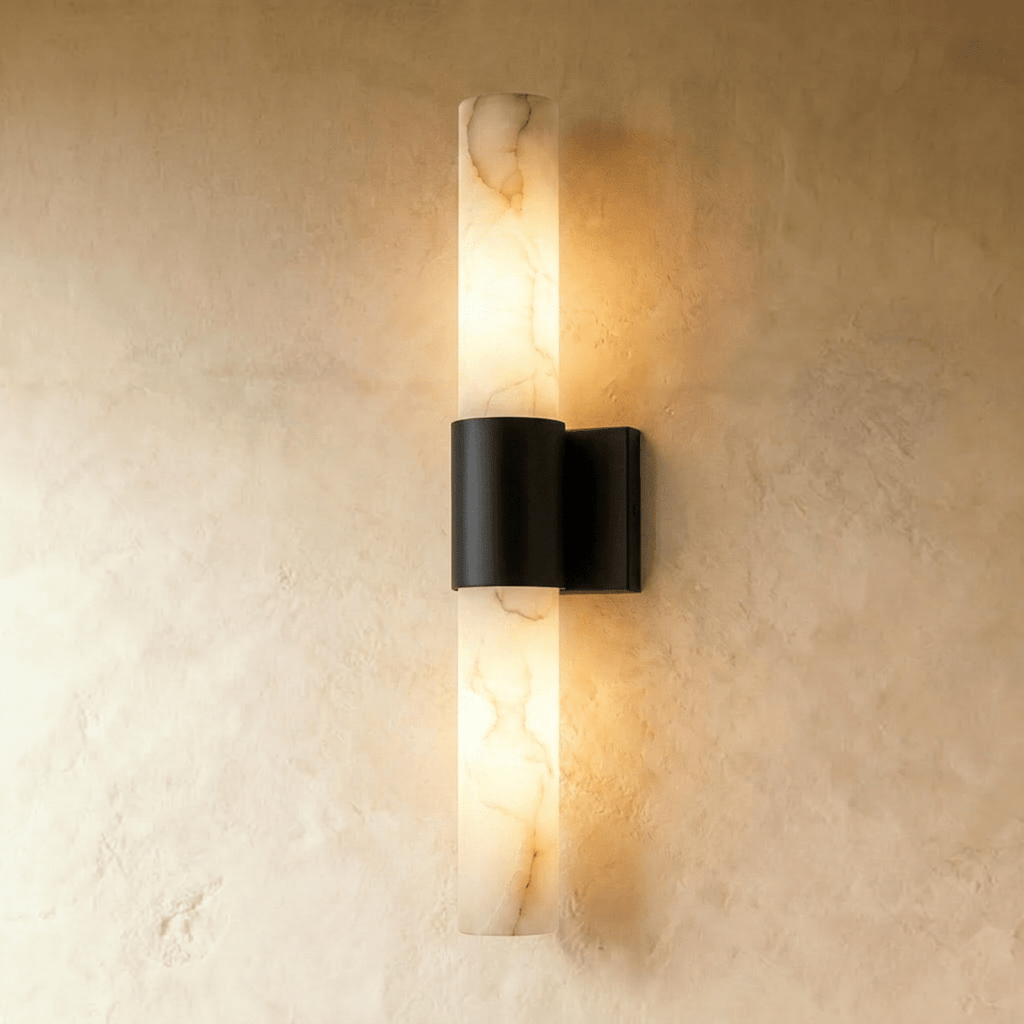 Clérachic 60 cm wall sconce with a glowing veined alabaster column and a matt black metal band on a limewash wall.