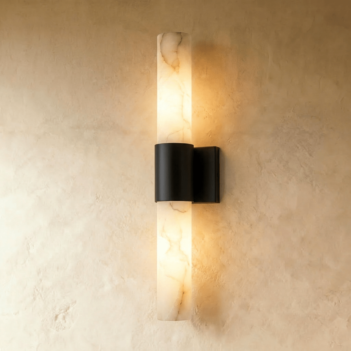 Clérachic 60 cm wall sconce with a glowing veined alabaster column and a matt black metal band on a limewash wall.