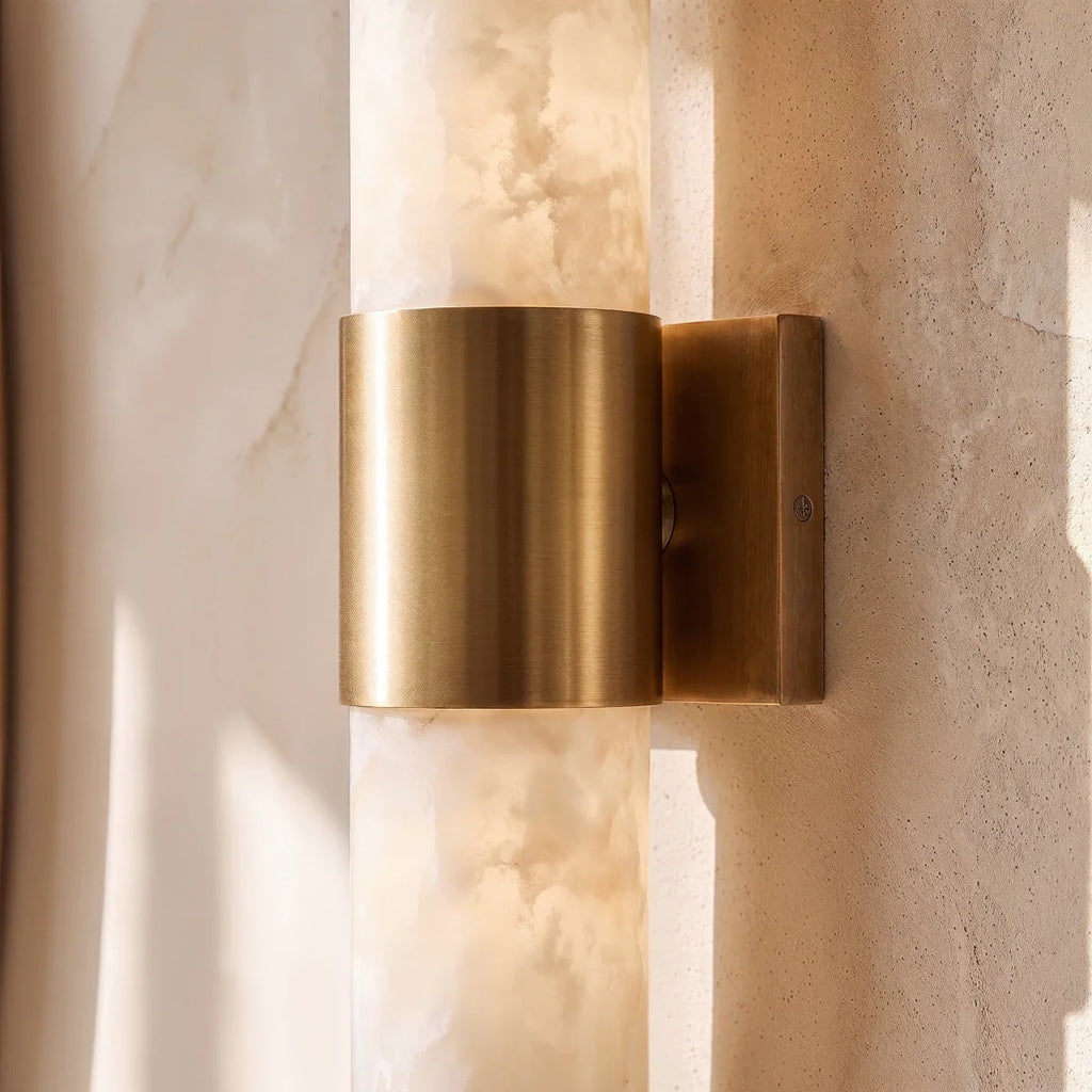 Close view of the Clérachic brushed brass band and wall plate, with the cloudy alabaster column glowing behind it.